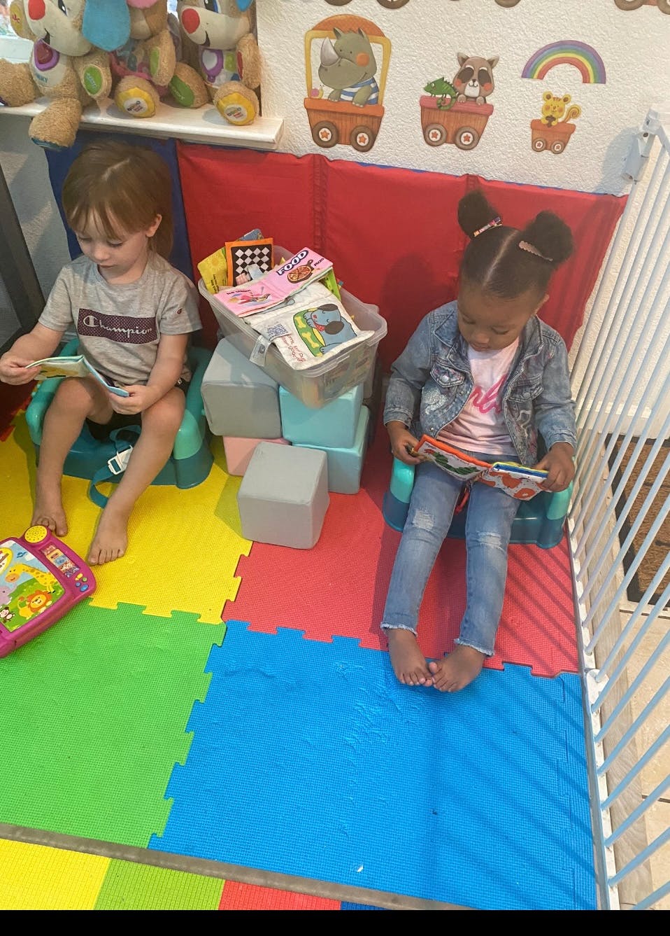 Two children sitting in seats on a play mat reading books