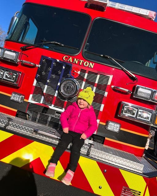 Child sitting on the front bumper of a fire truck