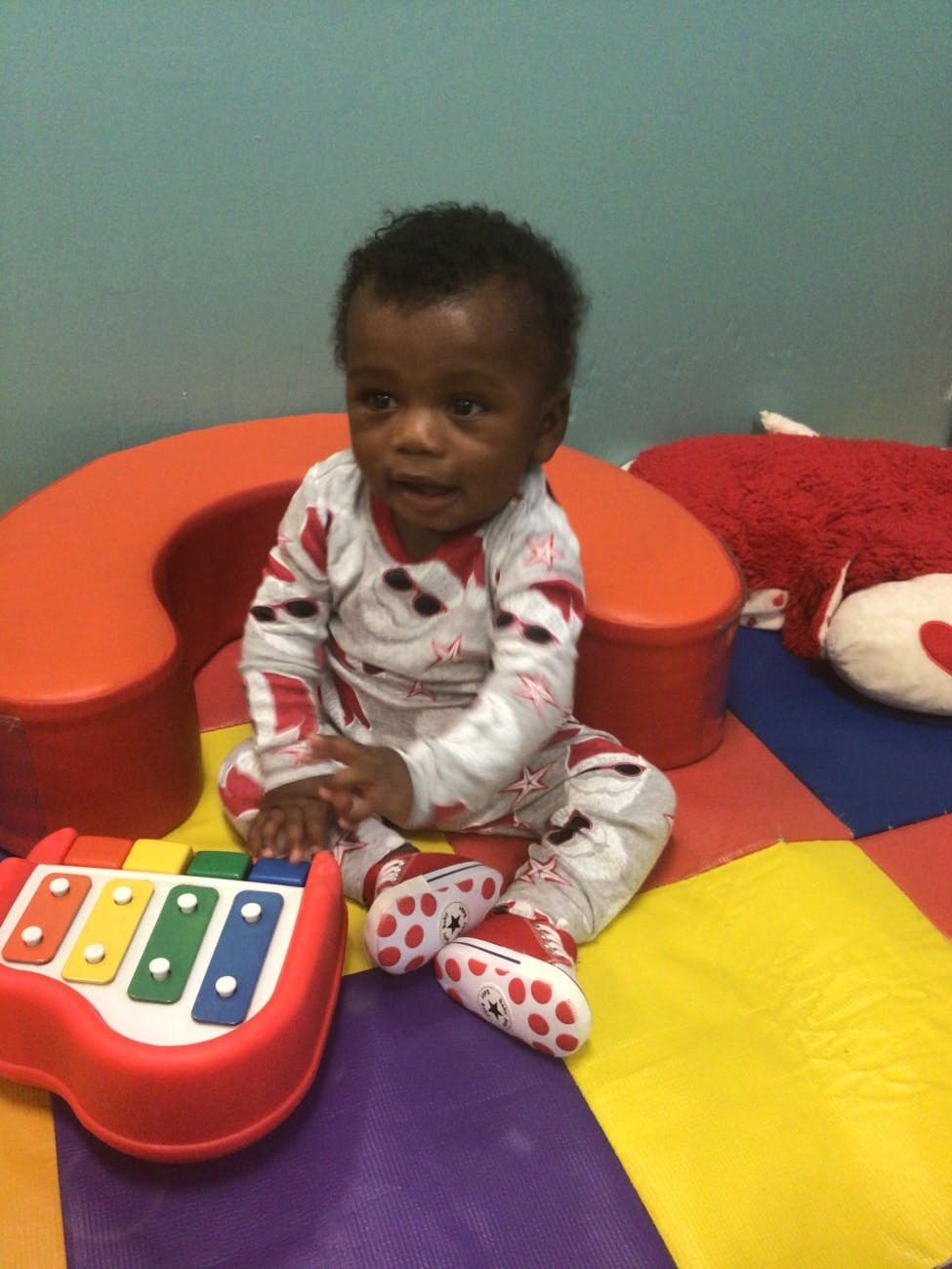 Child sitting on a colorful mat next to a toy xylophone