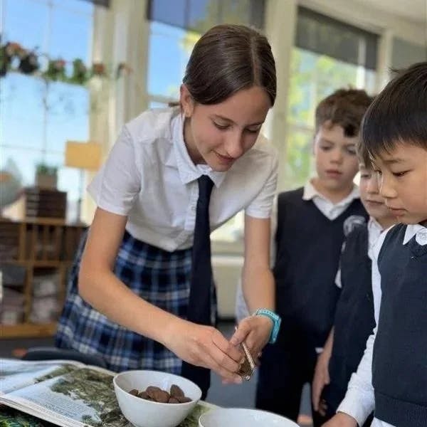 Teen showing something small to children in a classroom