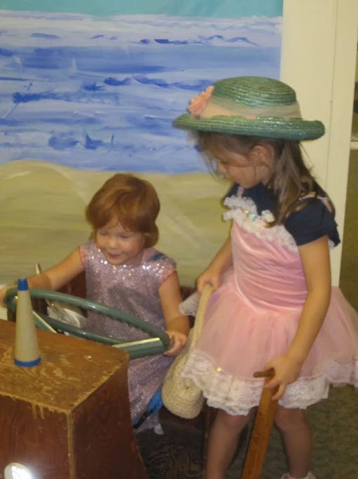 Two children playing, one holding a steering wheel, the other standing