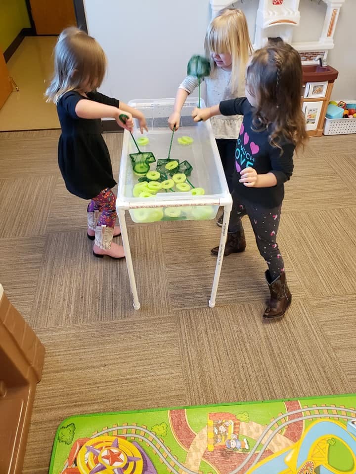 Three children playing with nets and green objects in a water table