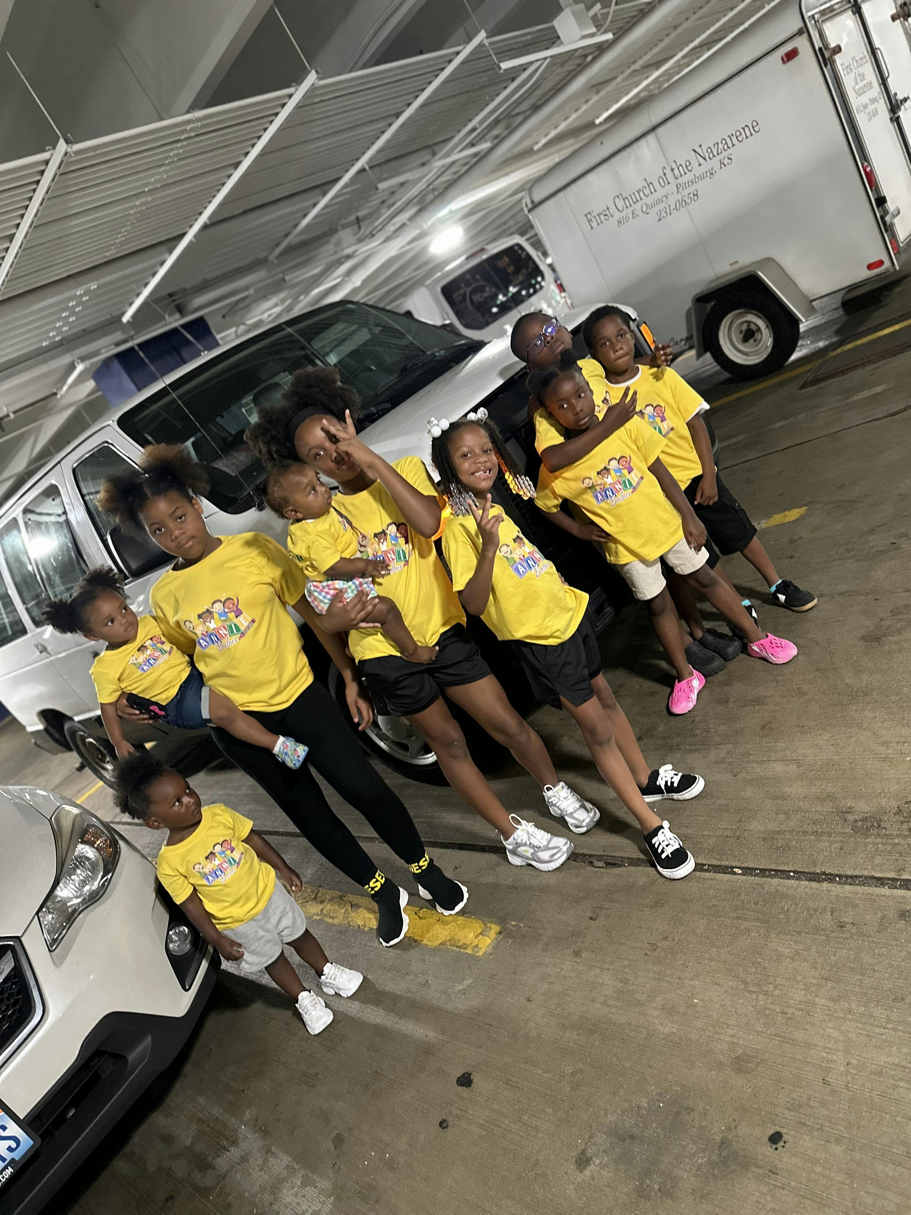 Group of children and teens in matching yellow t-shirts posing in a parking garage