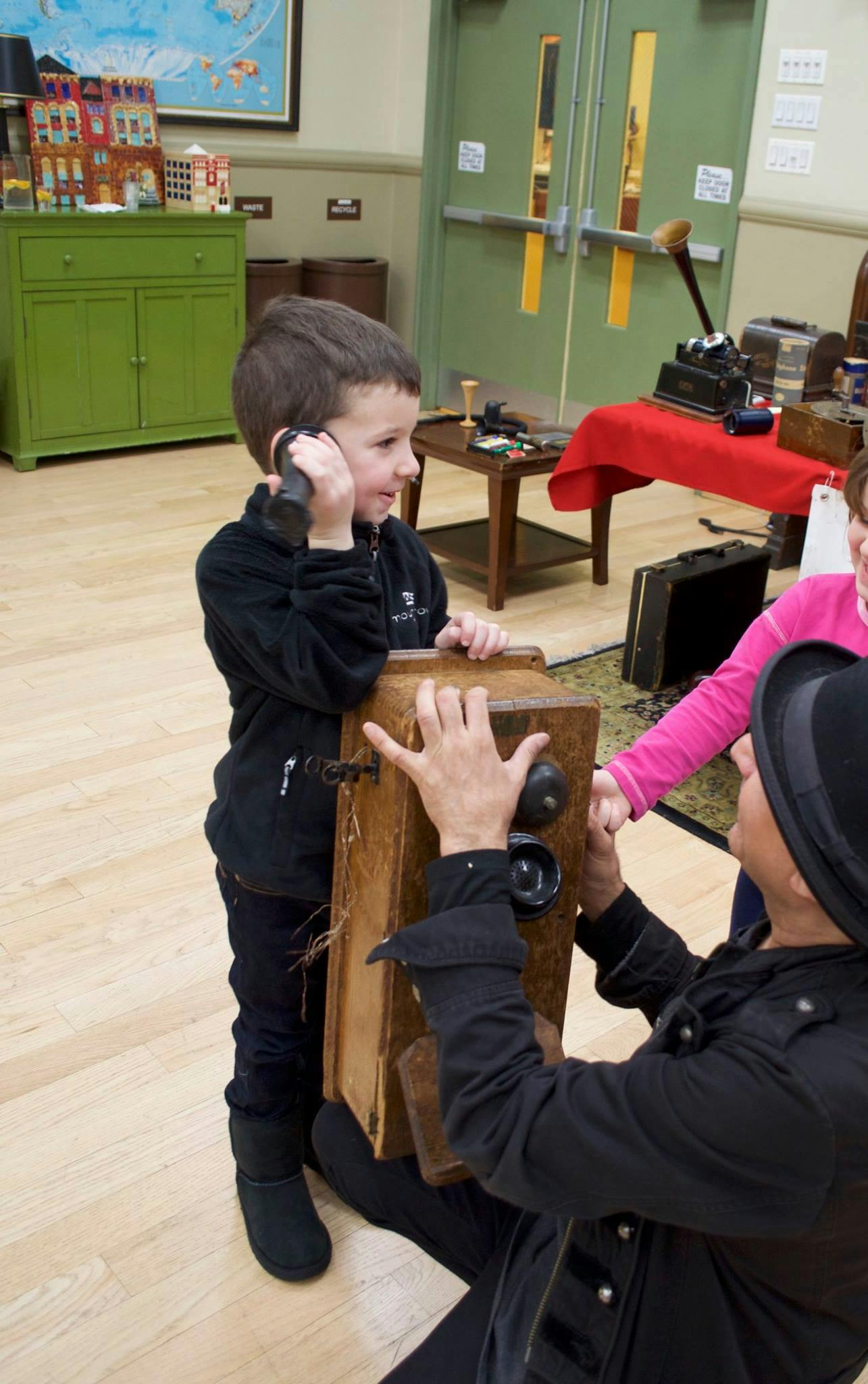 Child holding a phone receiver to their ear, person kneeling next to them