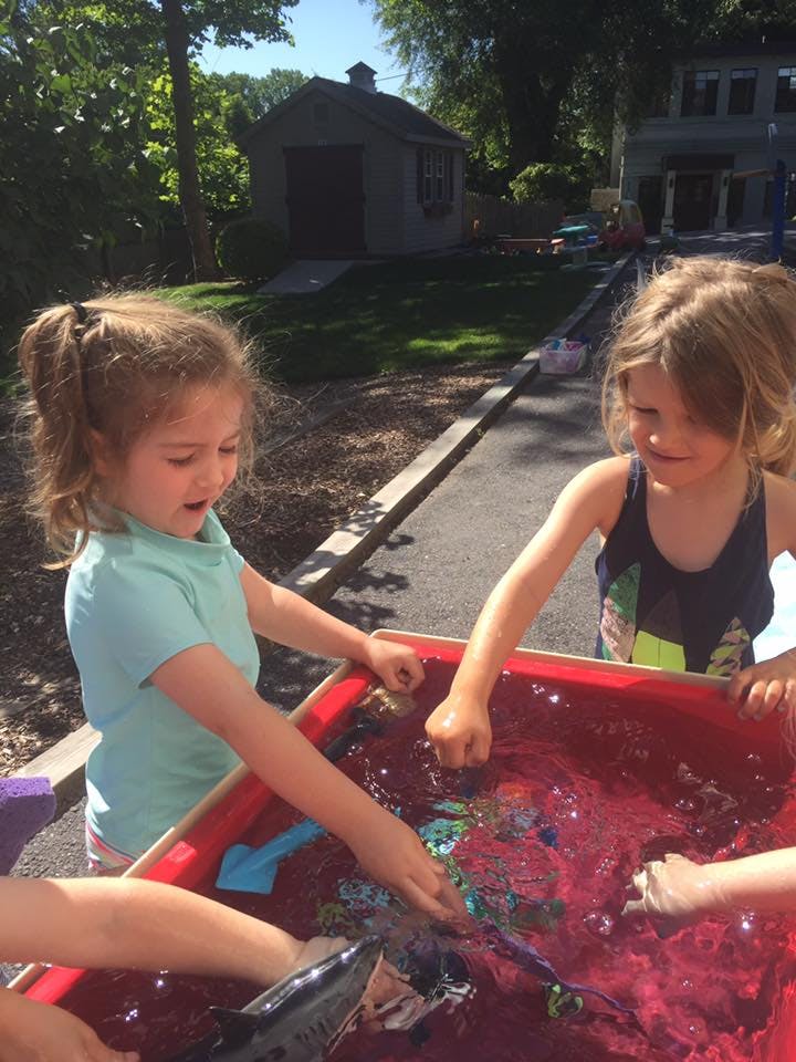 Two children playing in a red water table outdoors