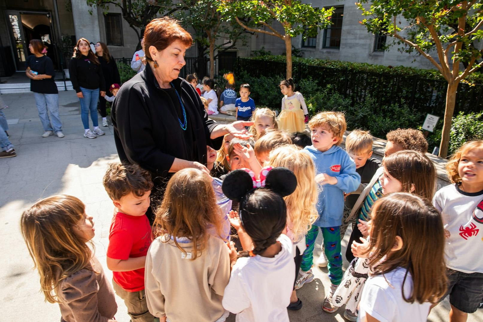 Adult person with dark hair, children gathered around her outside
