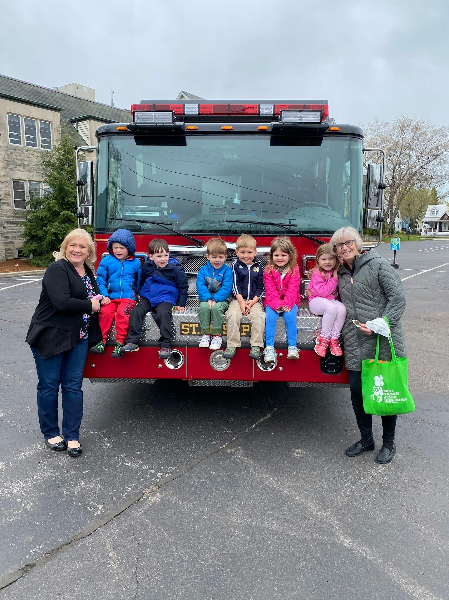 Two people and five children sitting on the front of a fire truck