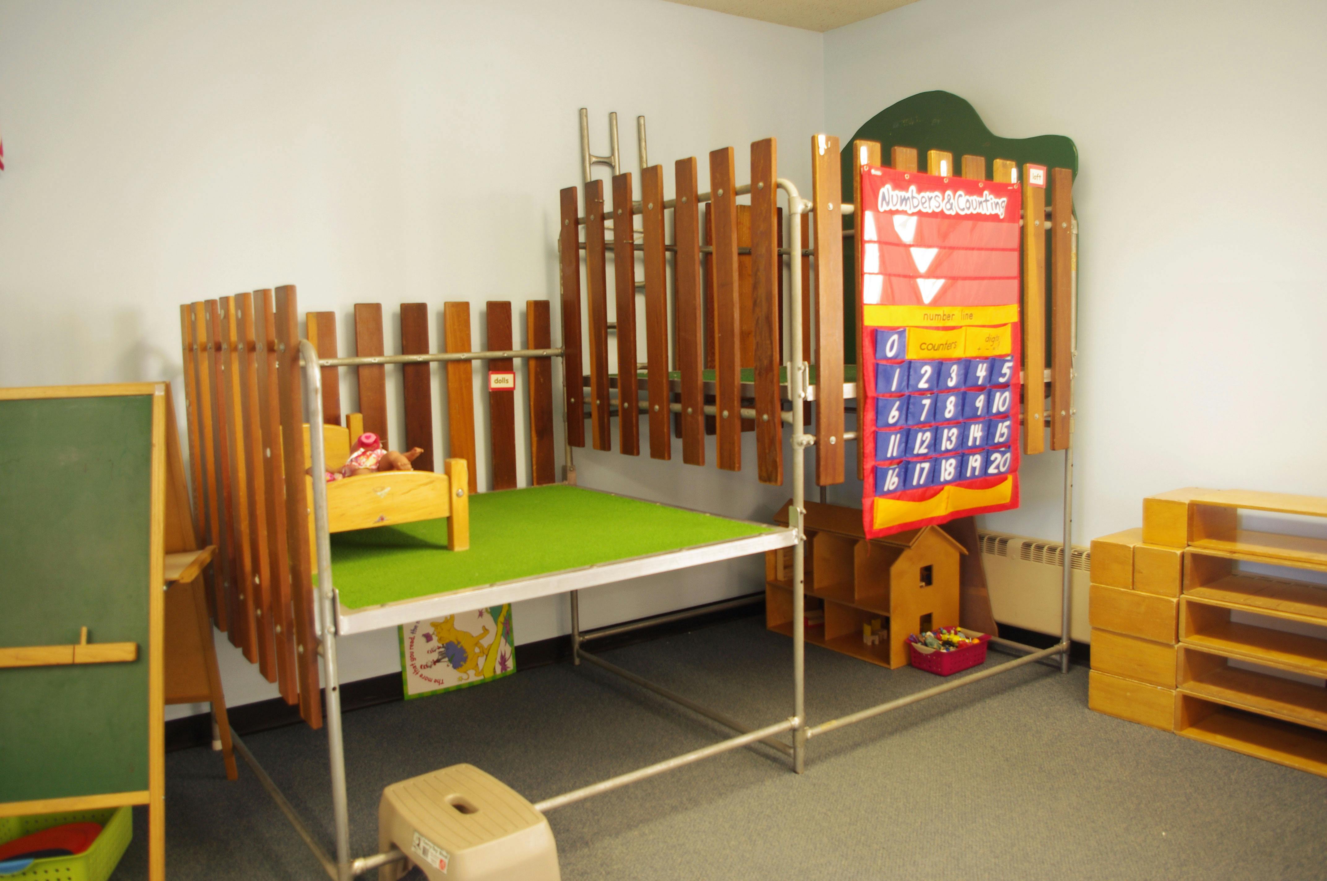 Play area with a green mat, wooden fence-like structures, and a calendar