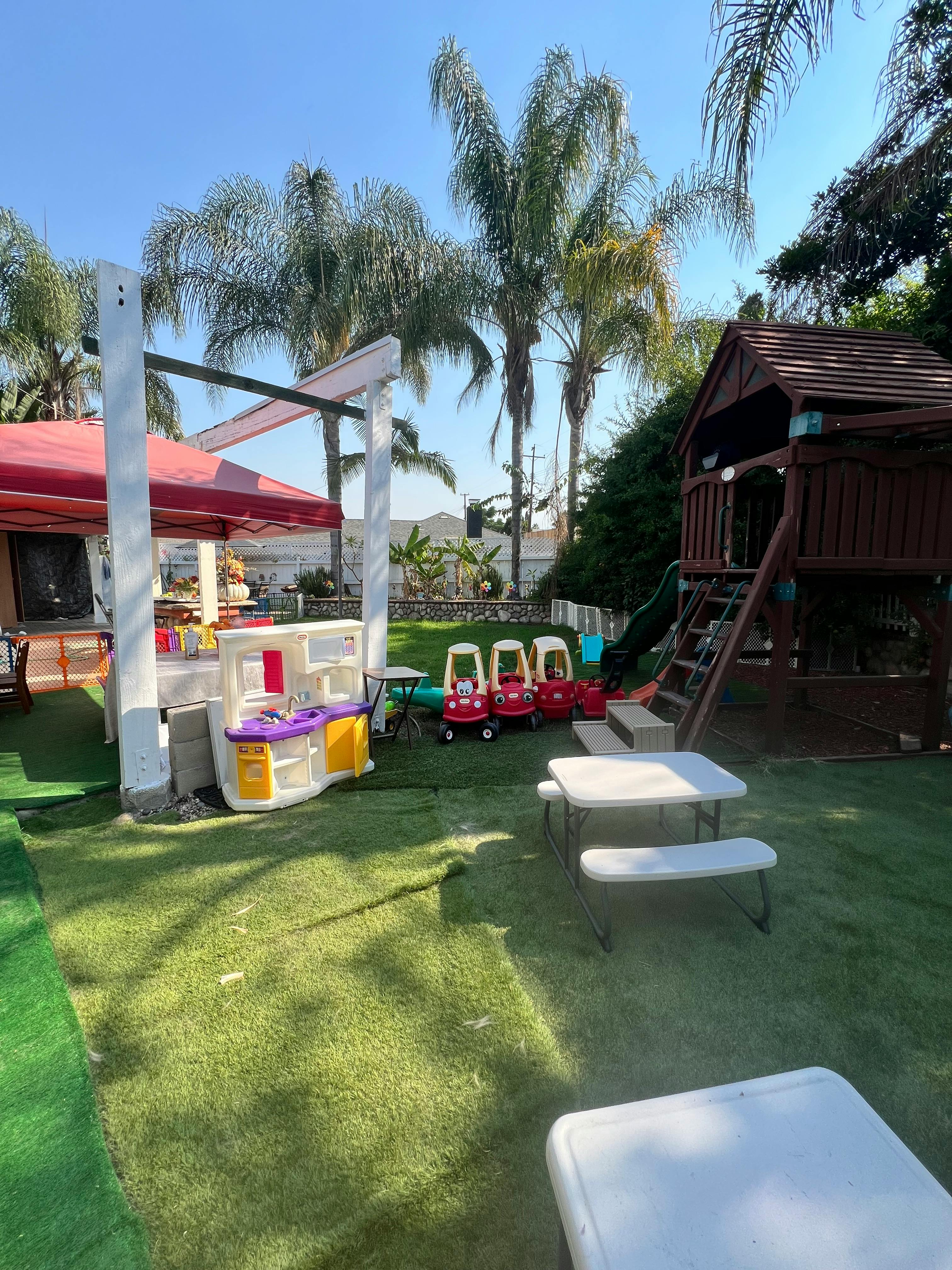 Outdoor play area with artificial grass, playhouse, toy cars, and picnic tables