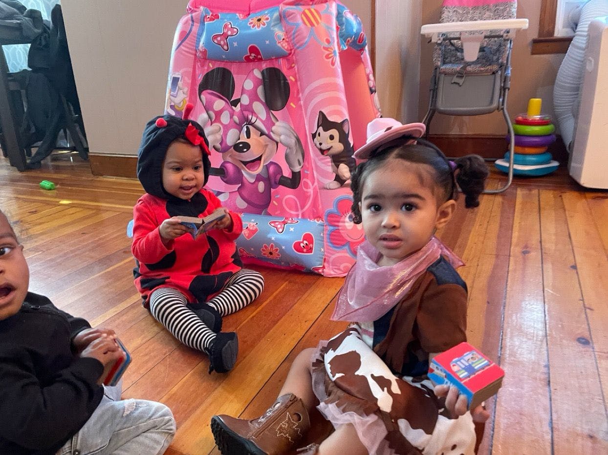 Two children sitting on a wooden floor, one in a ladybug costume