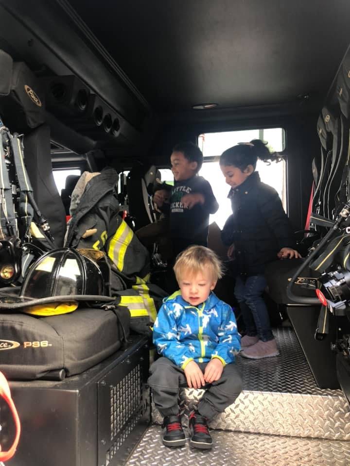 Three children sitting inside a vehicle with firefighter gear