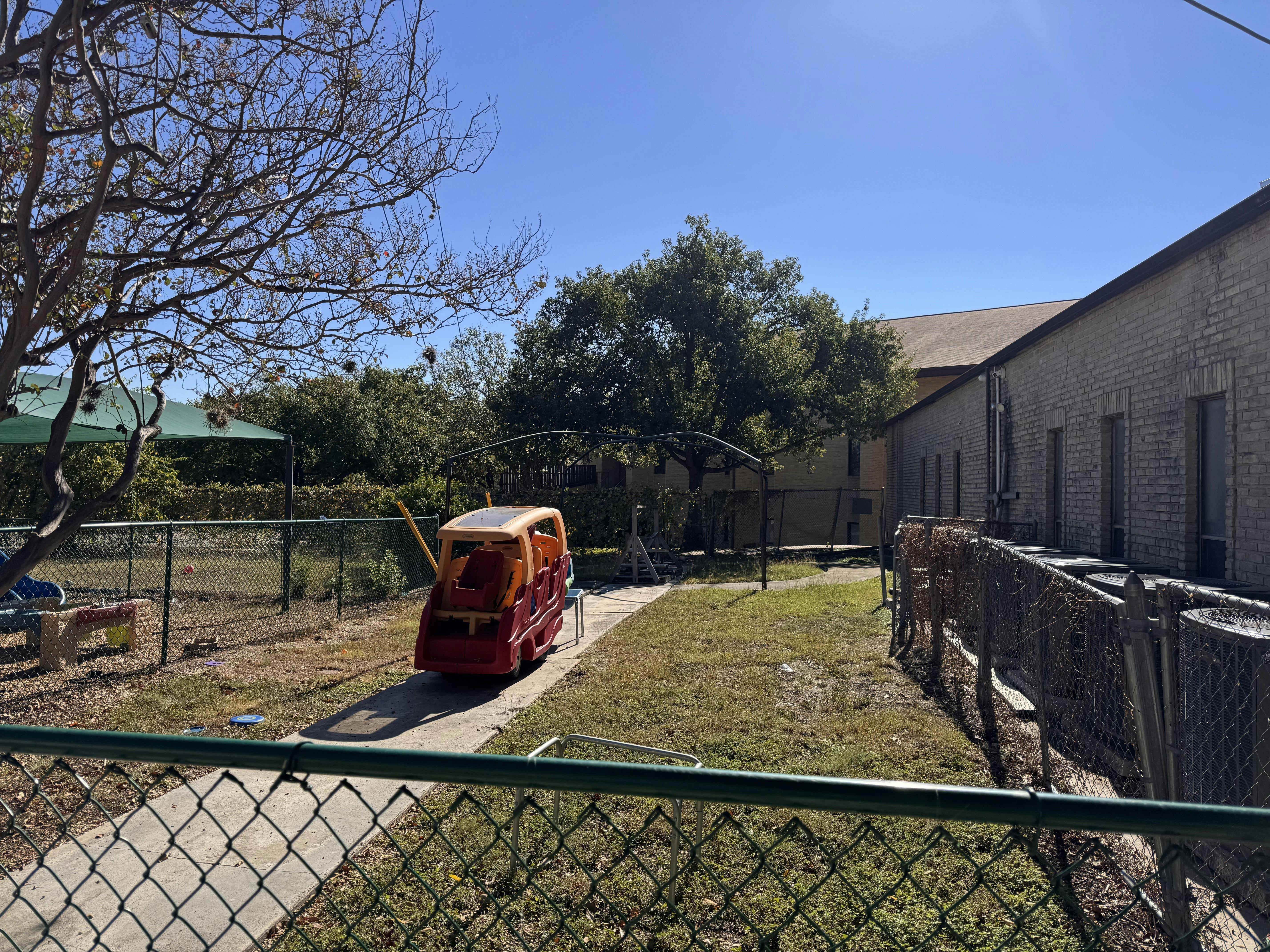 Plastic toy train on a sidewalk in a fenced outdoor play area