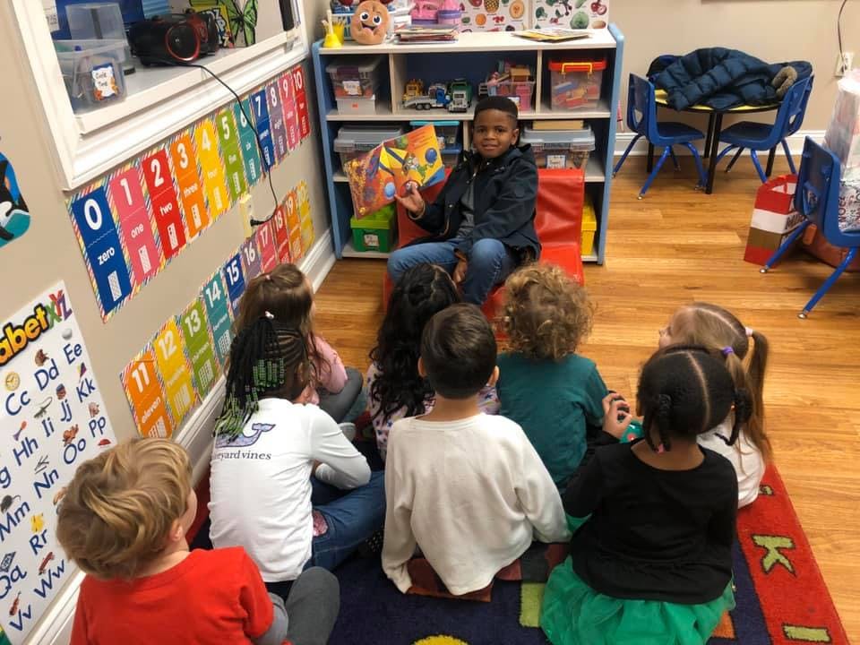 Child reading a book to a group of children sitting on the floor