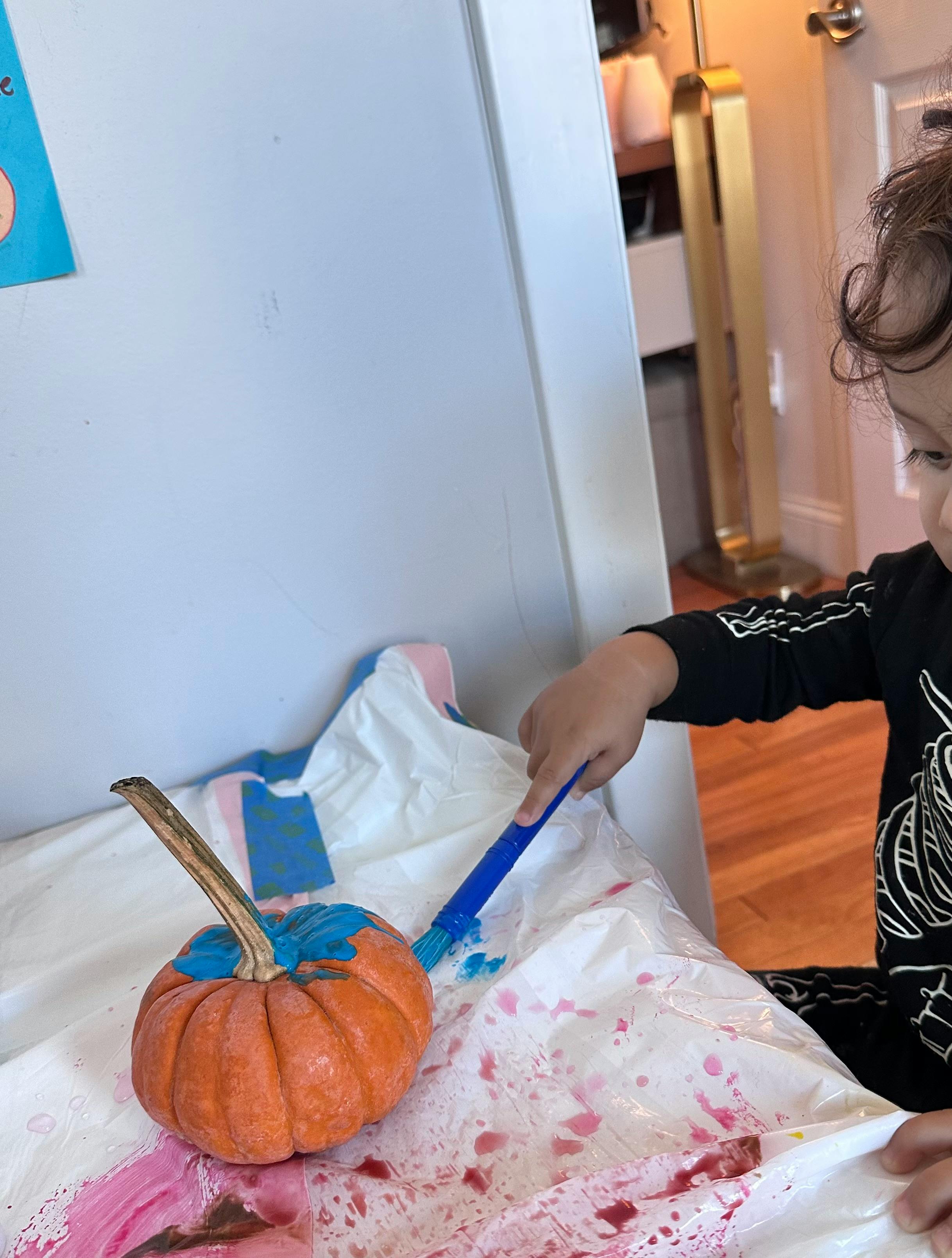 Child painting a pumpkin blue with blue paint