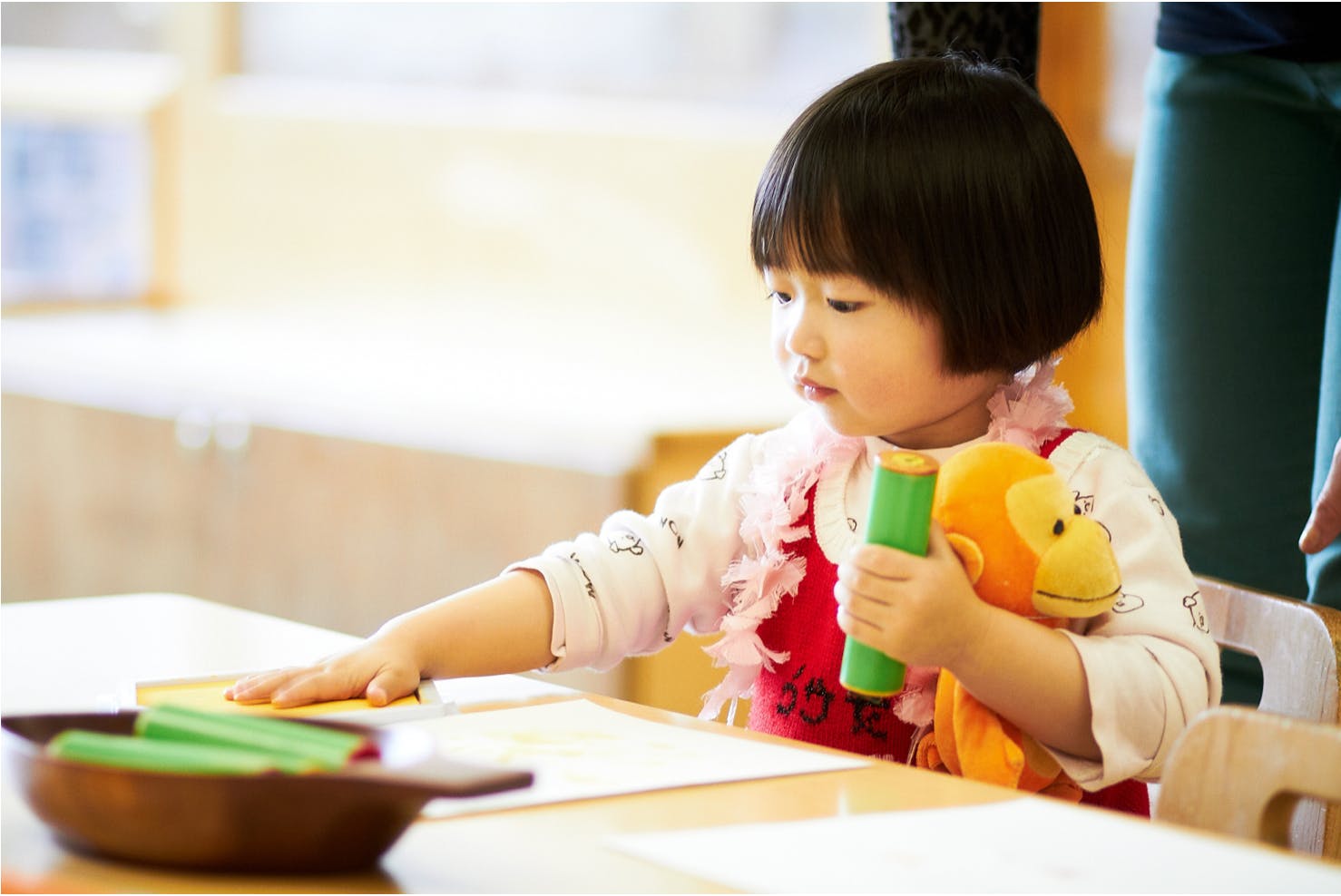 Child at a table with a toy and a bowl of green objects
