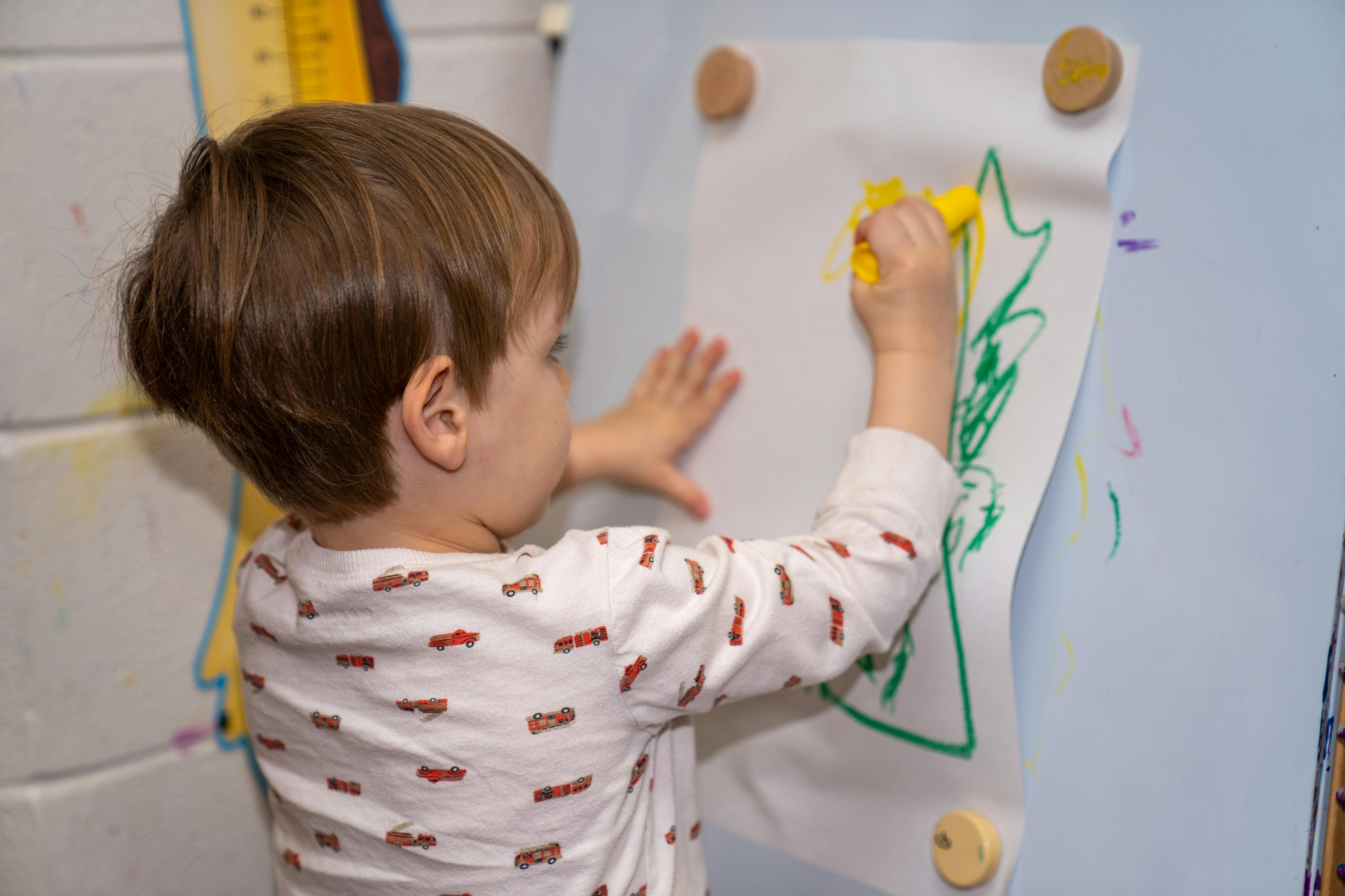 Child drawing on paper with a yellow crayon