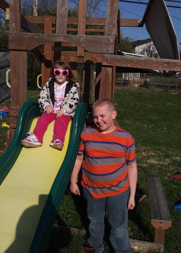 Child in pink sunglasses sitting on a slide next to a standing child