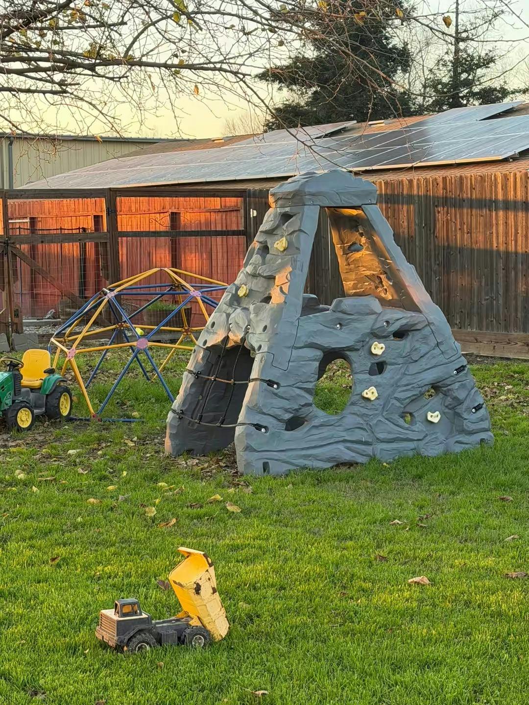 Playground equipment including a climbing structure, dome, and toy tractor on grass
