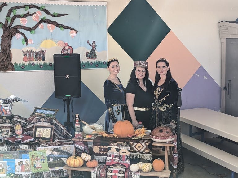 Three women in traditional attire next to a decorated table with pumpkins