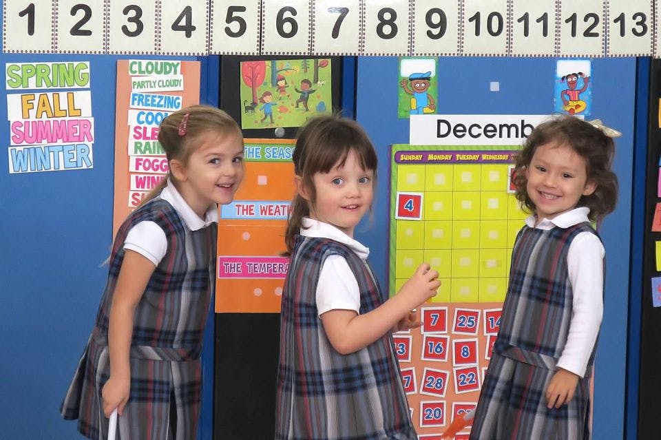 Three children in plaid uniforms in a classroom