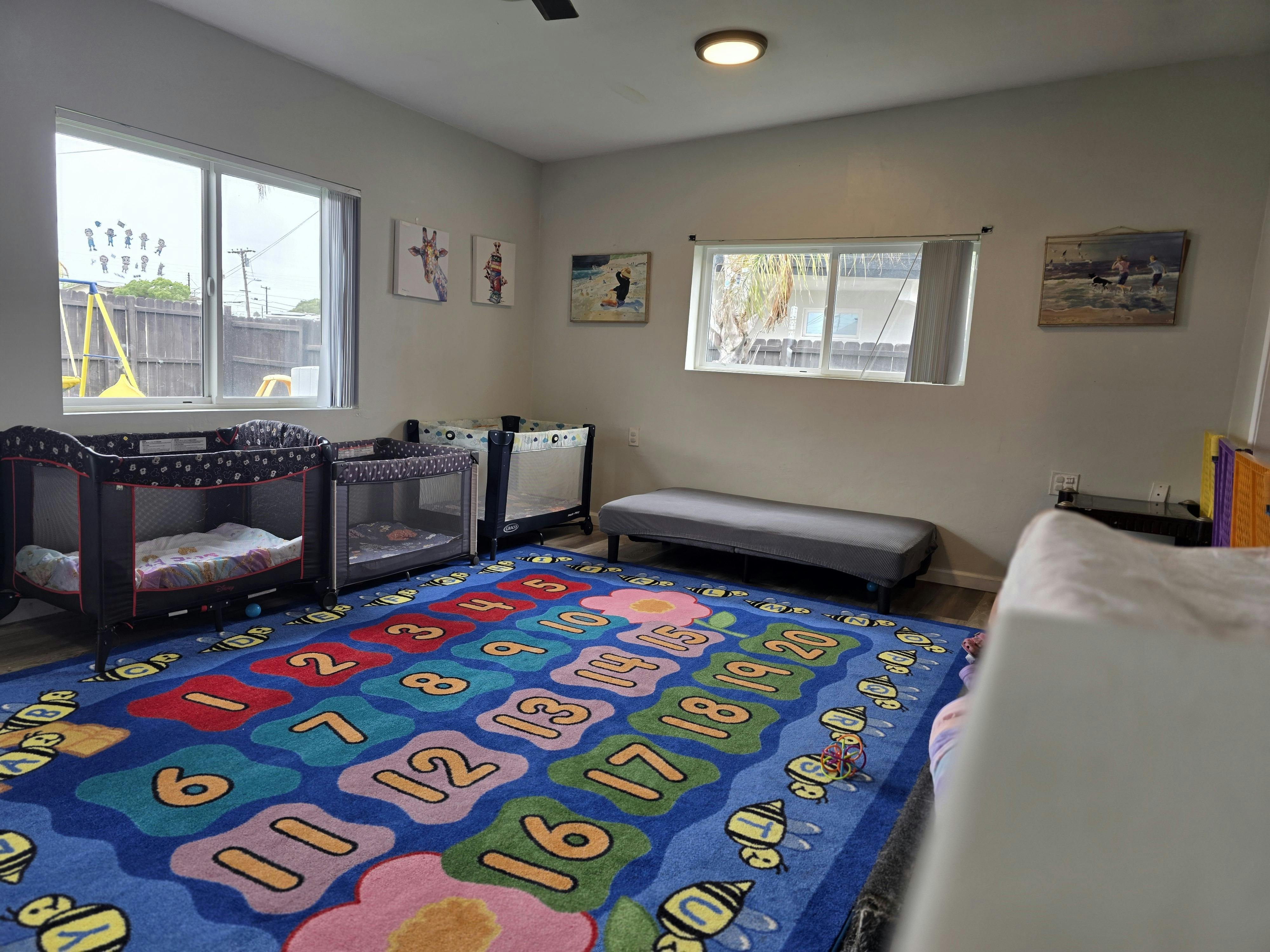 Room with a colorful number rug, cribs, and windows