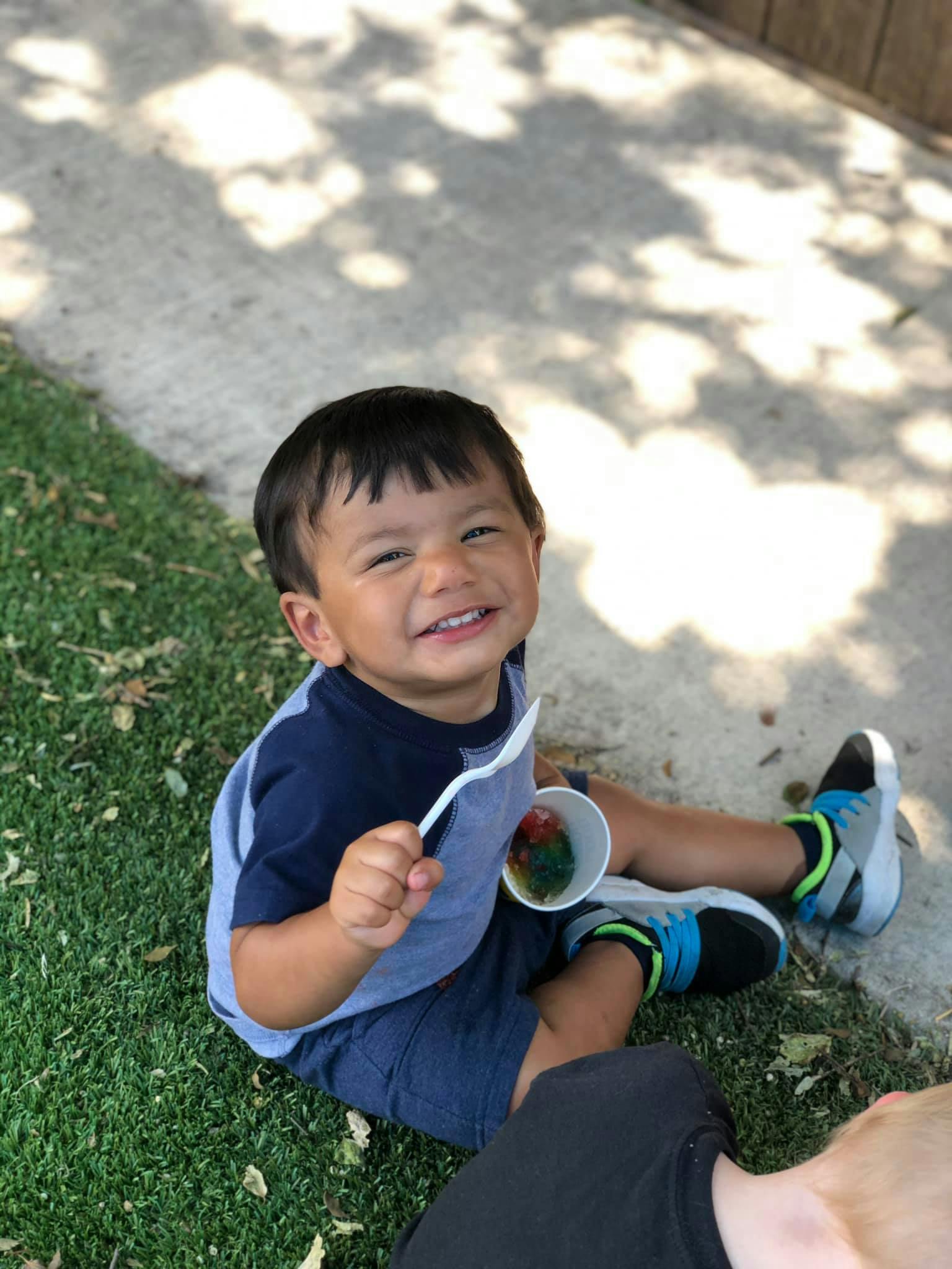 Child sitting on grass holding a spoon and cup