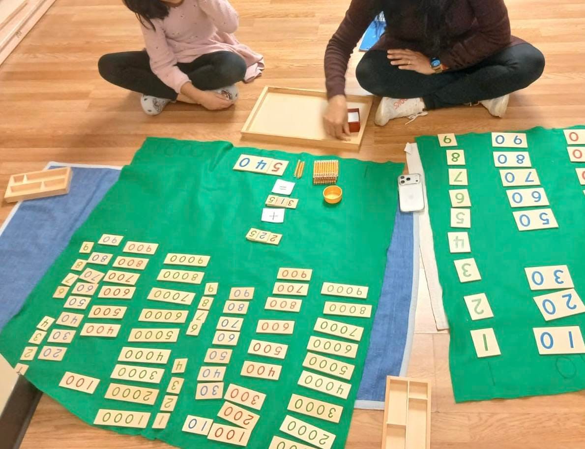 People doing math with number cards and Montessori golden beads on green mats