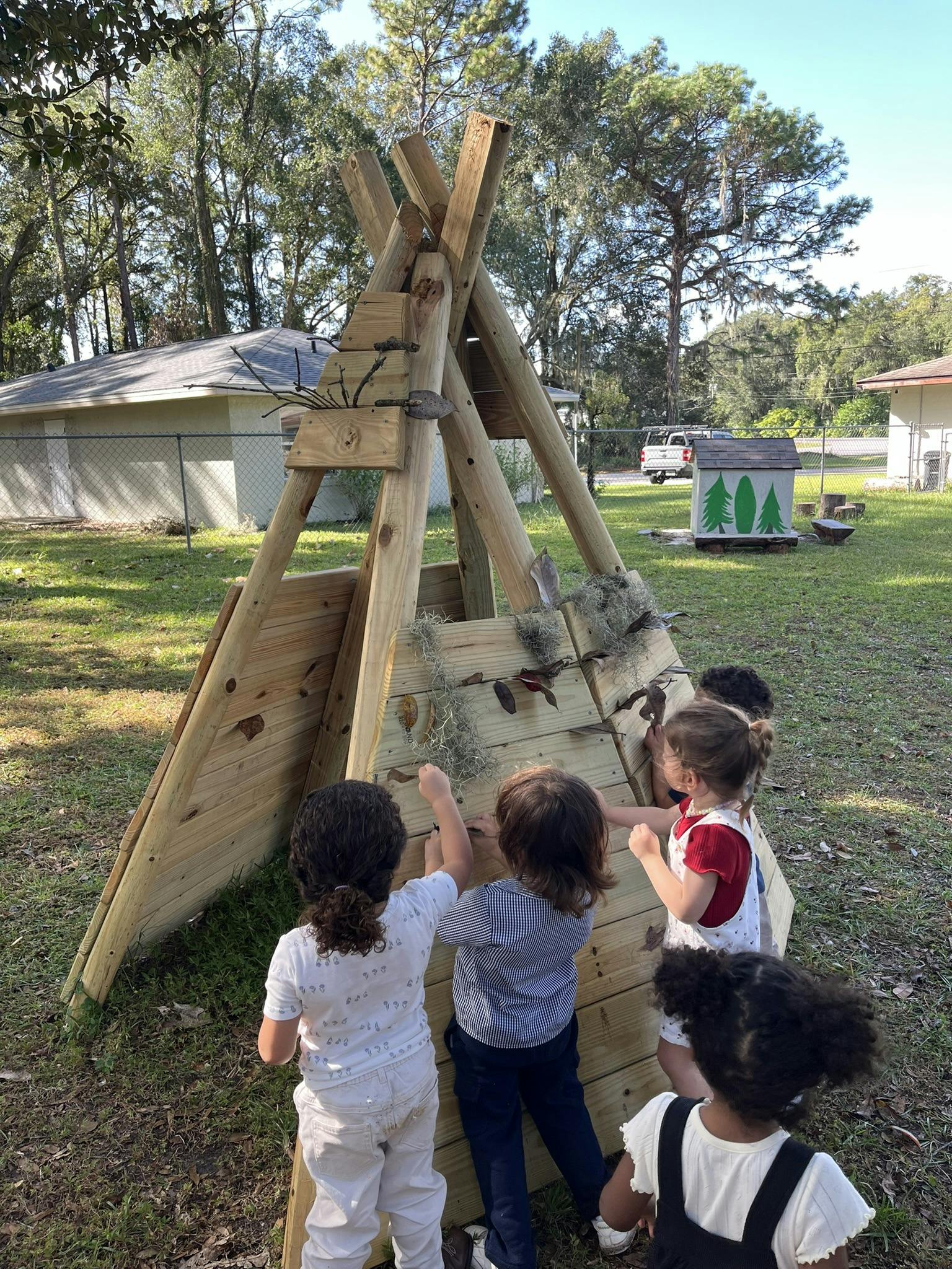 Children playing around a wooden teepee structure outdoors