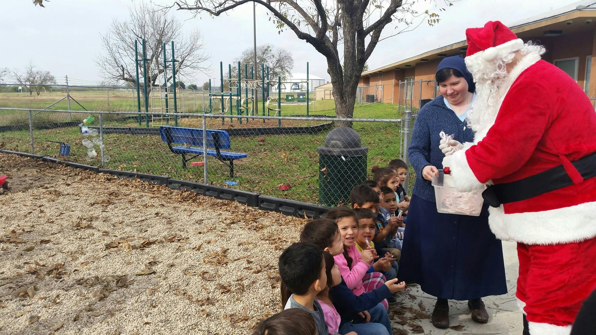 Person dressed as Santa Claus giving gifts to children with an adult