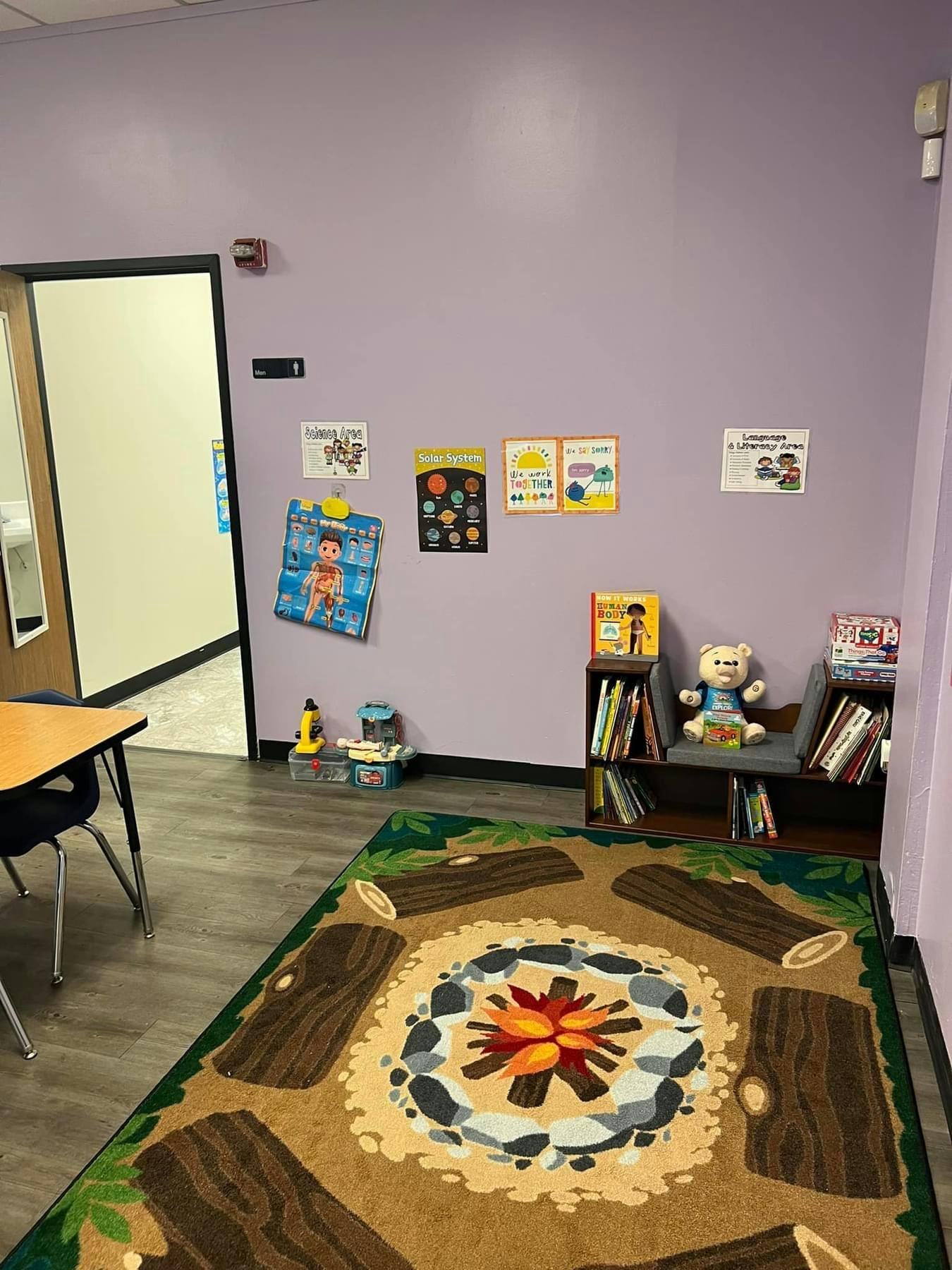 Classroom with a campfire-themed rug, bookshelves, and posters on a purple wall