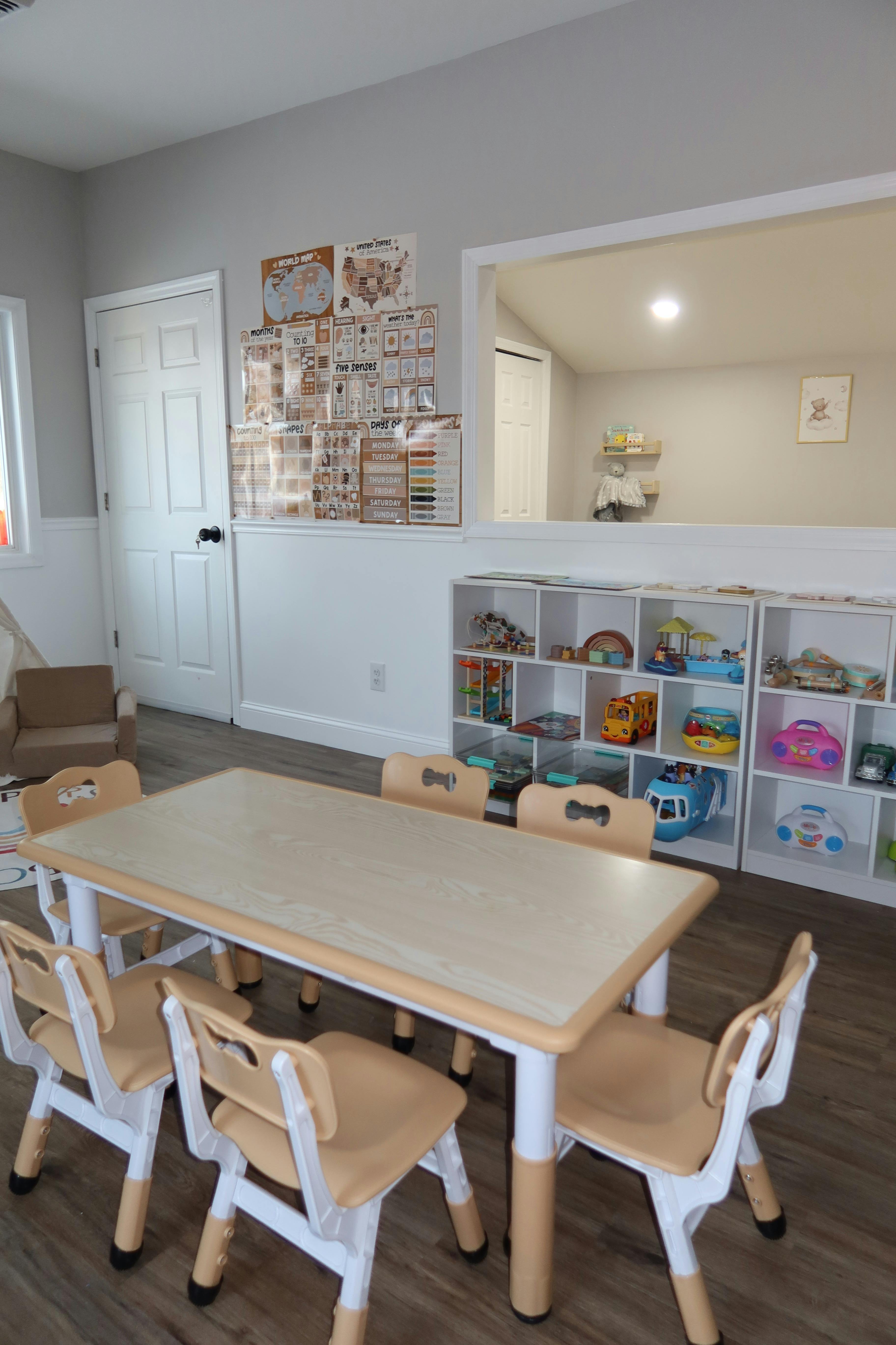 Children's classroom with a long table and chairs, shelves of toys, and educational posters