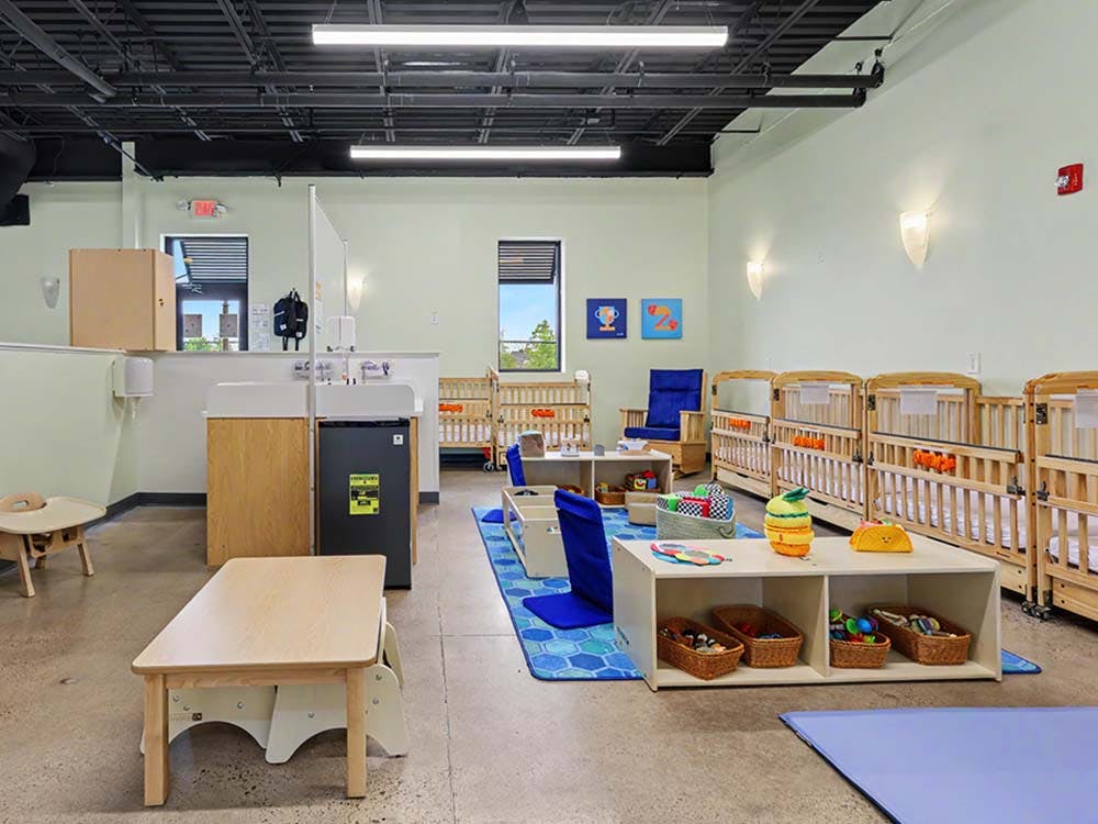 An empty nursery room with multiple cribs, changing station, and play areas