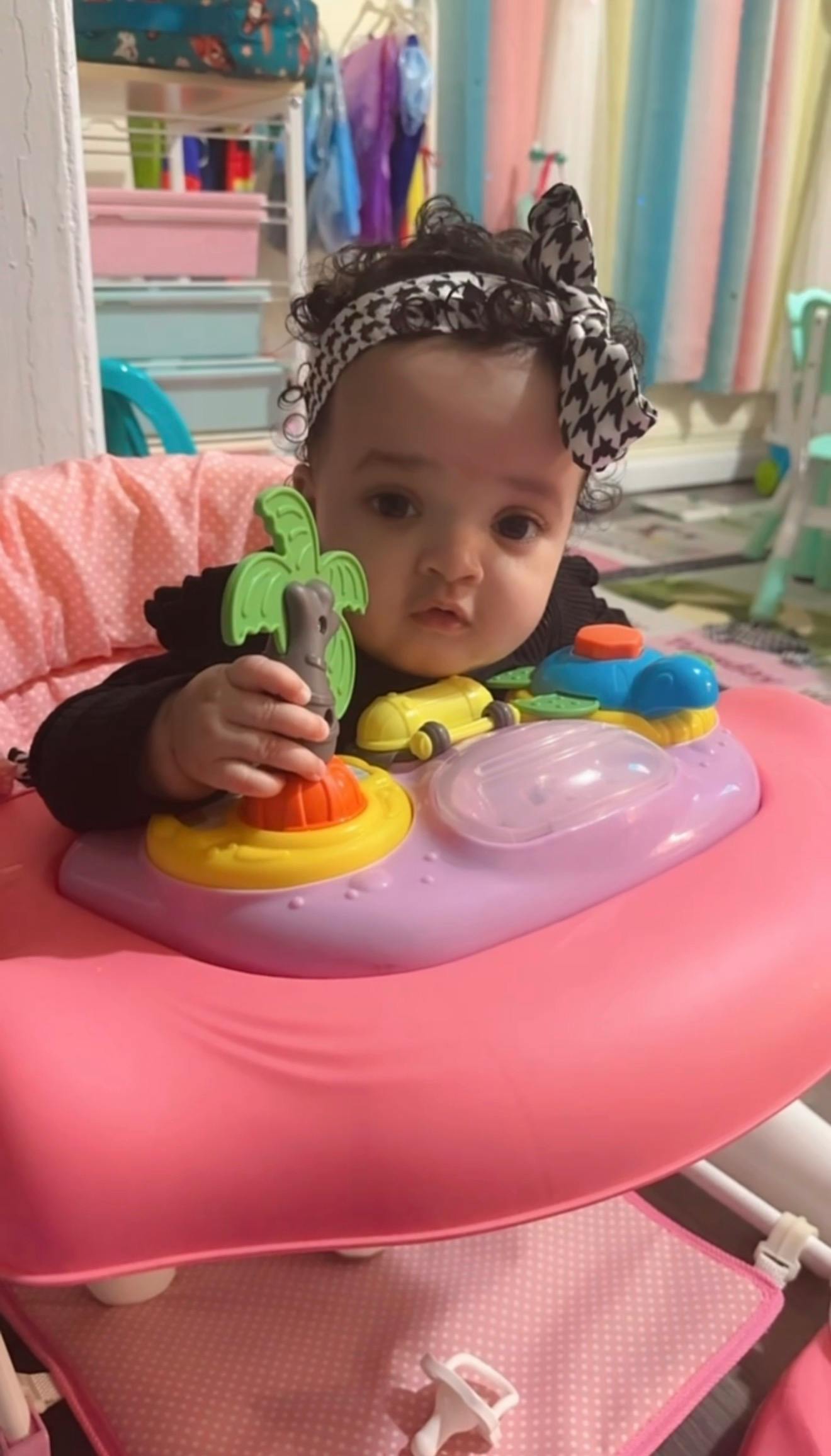 Child in a pink high chair playing with a green and orange toy