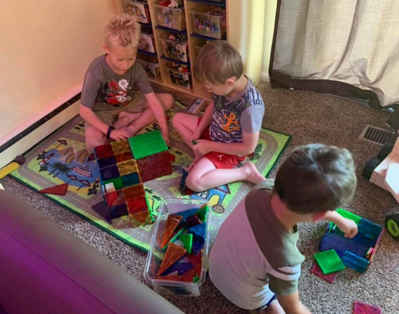 Three children playing with colorful magnetic tiles on a rug