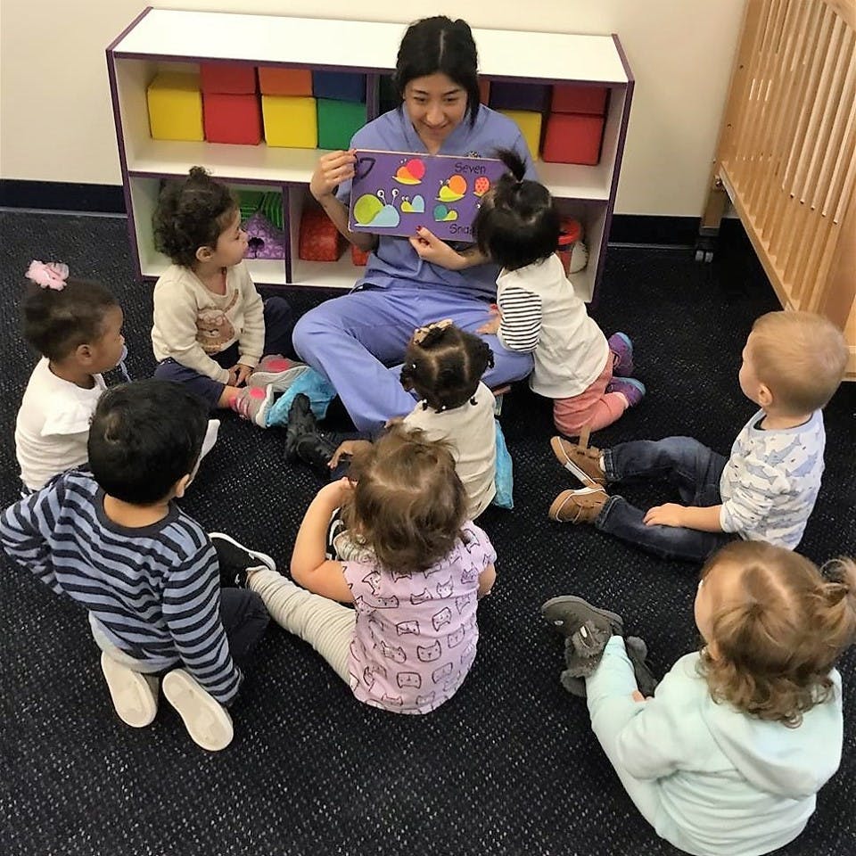 Person reading a book to a group of children sitting on the floor