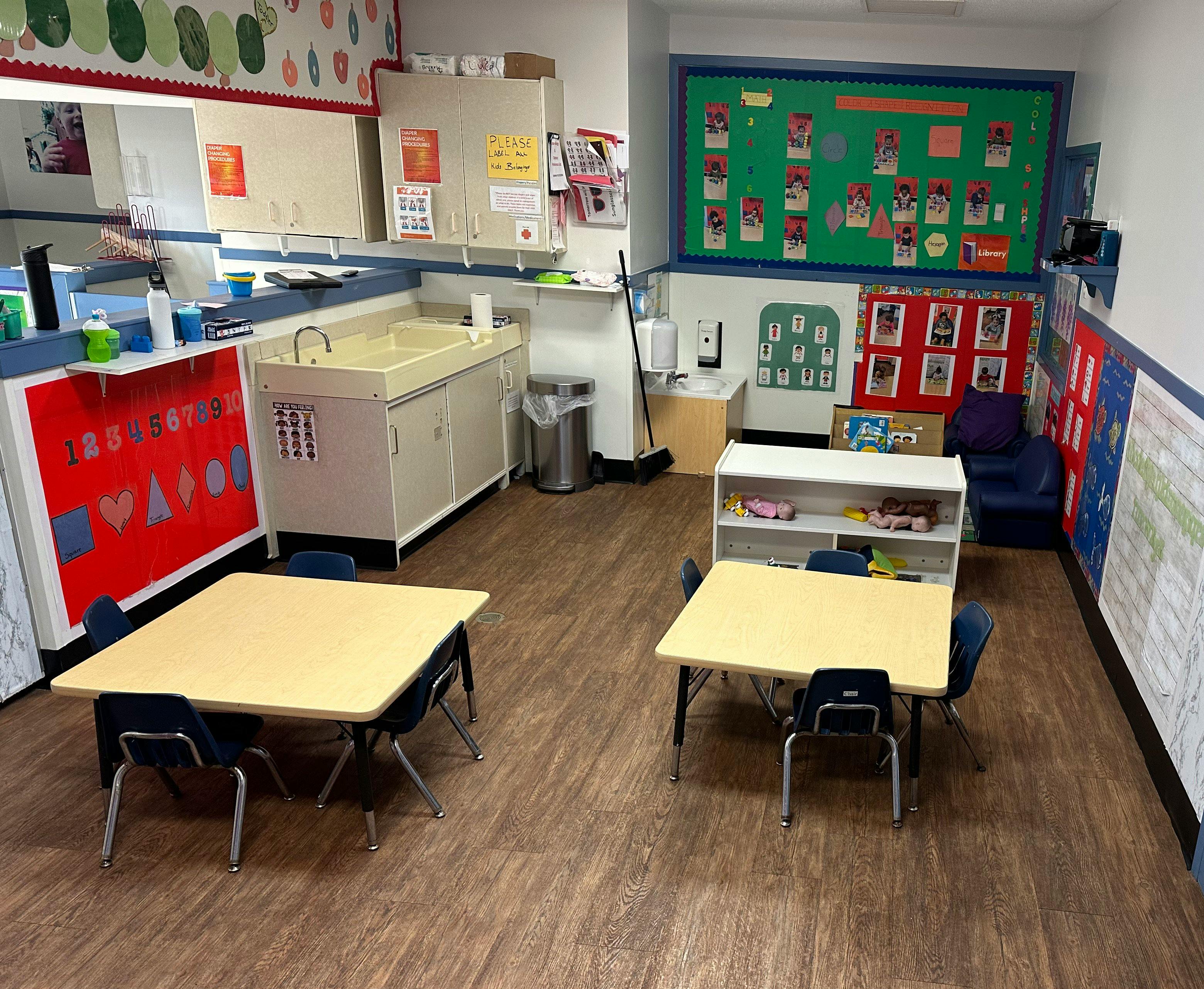 Classroom with small tables and chairs, diaper changing station, and learning posters