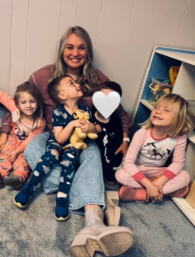 Person sitting with three children, one holding a stuffed animal