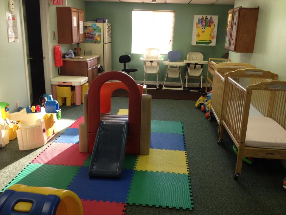 Indoor play area with colorful floor mats, a slide, and cribs