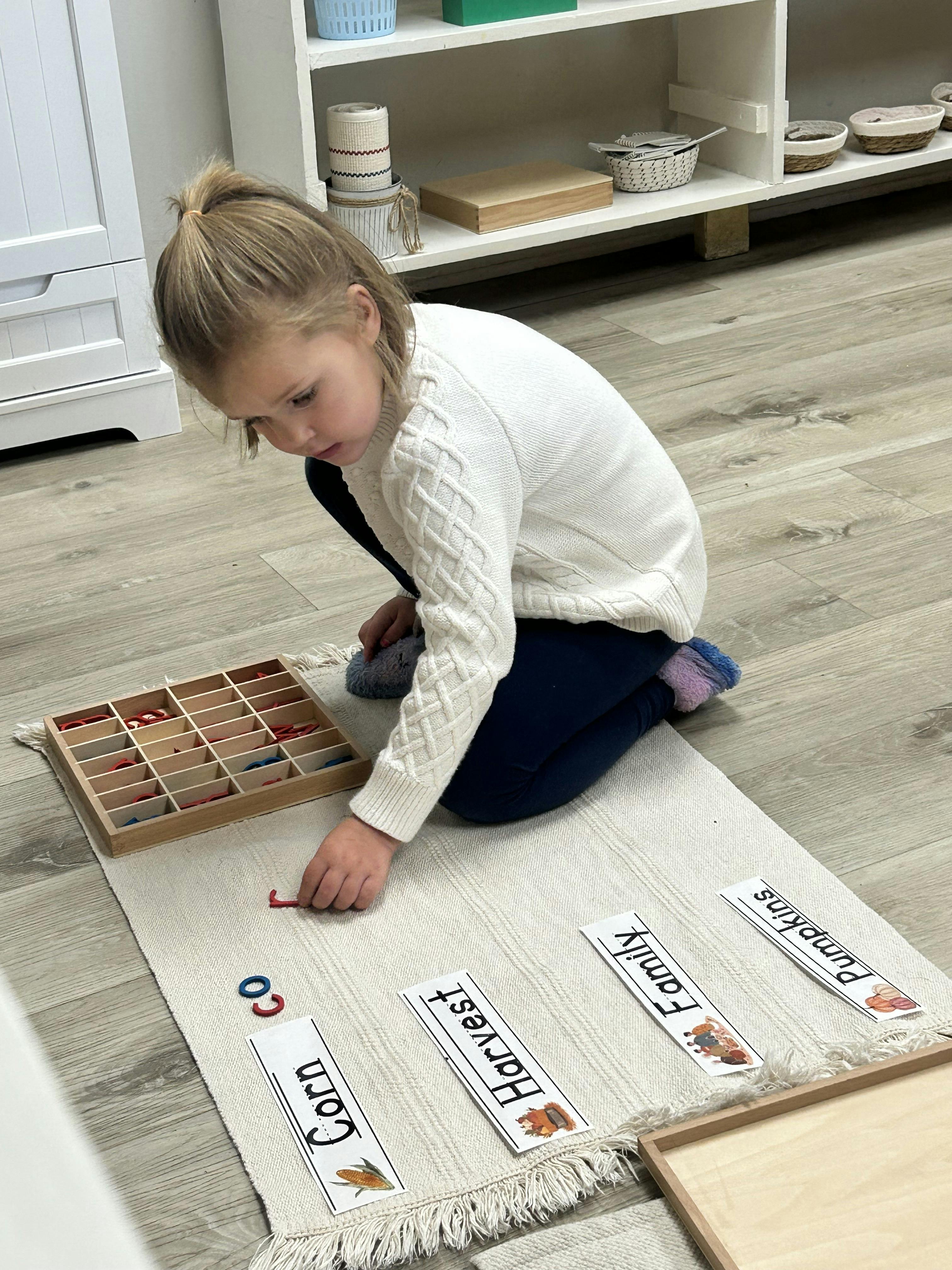Child on floor, arranging letter shapes next to word cards