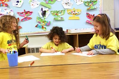 Three children drawing at a table in a classroom