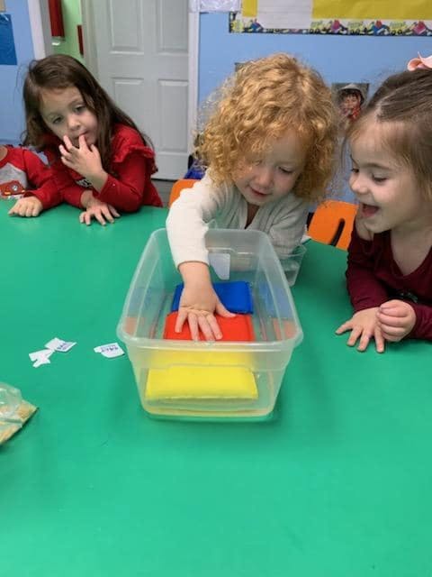 Three children playing with colorful blocks in a clear container