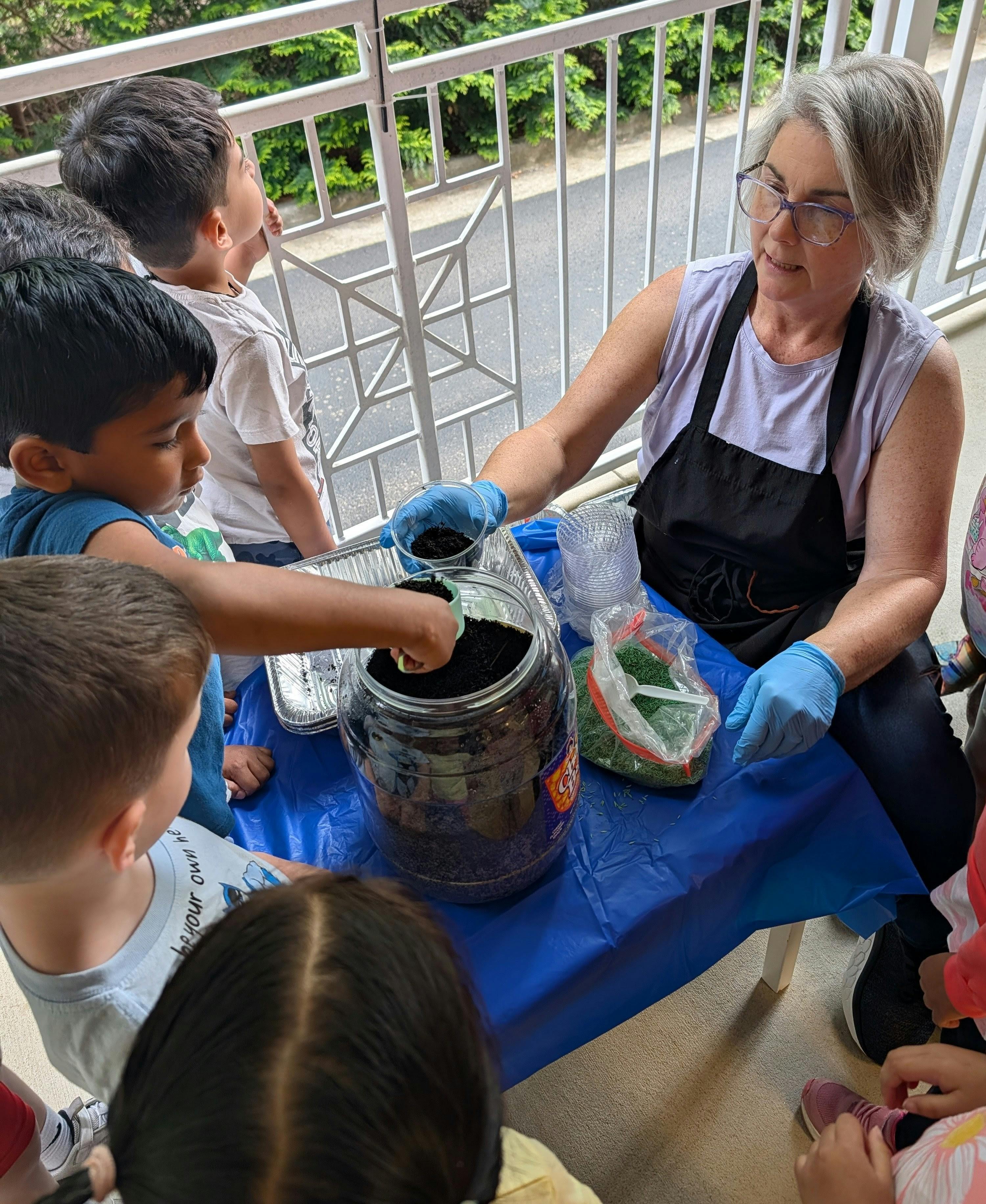 Adult in an apron and blue gloves helping children with a planting activity