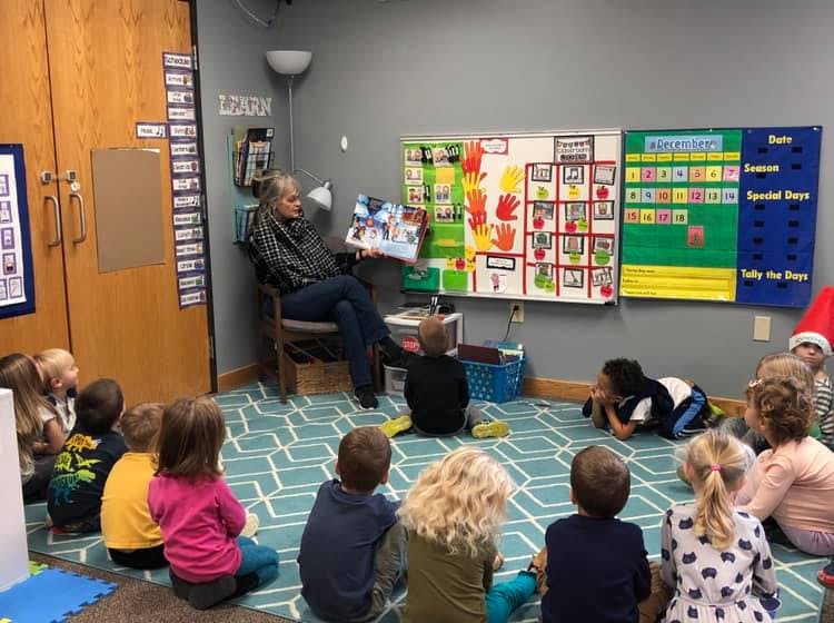 Person reading a book to a group of children in a classroom