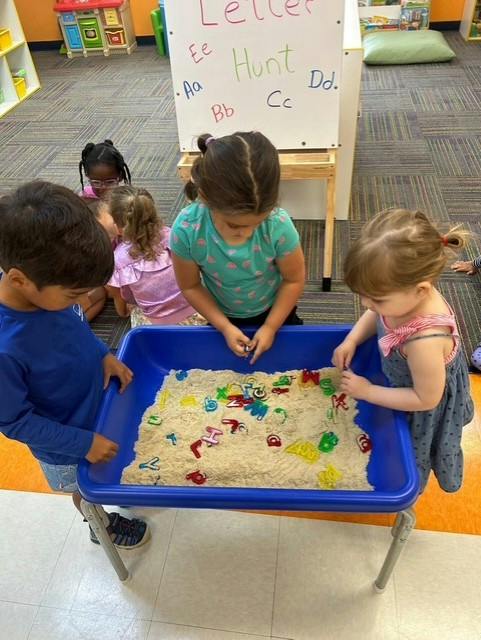 Children playing with plastic letters in a sand table