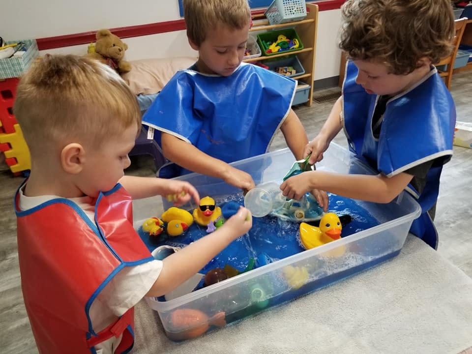 Three children playing with rubber ducks in a water bin