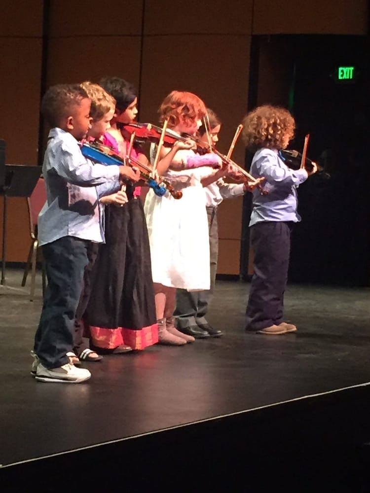 Children playing violins on a stage