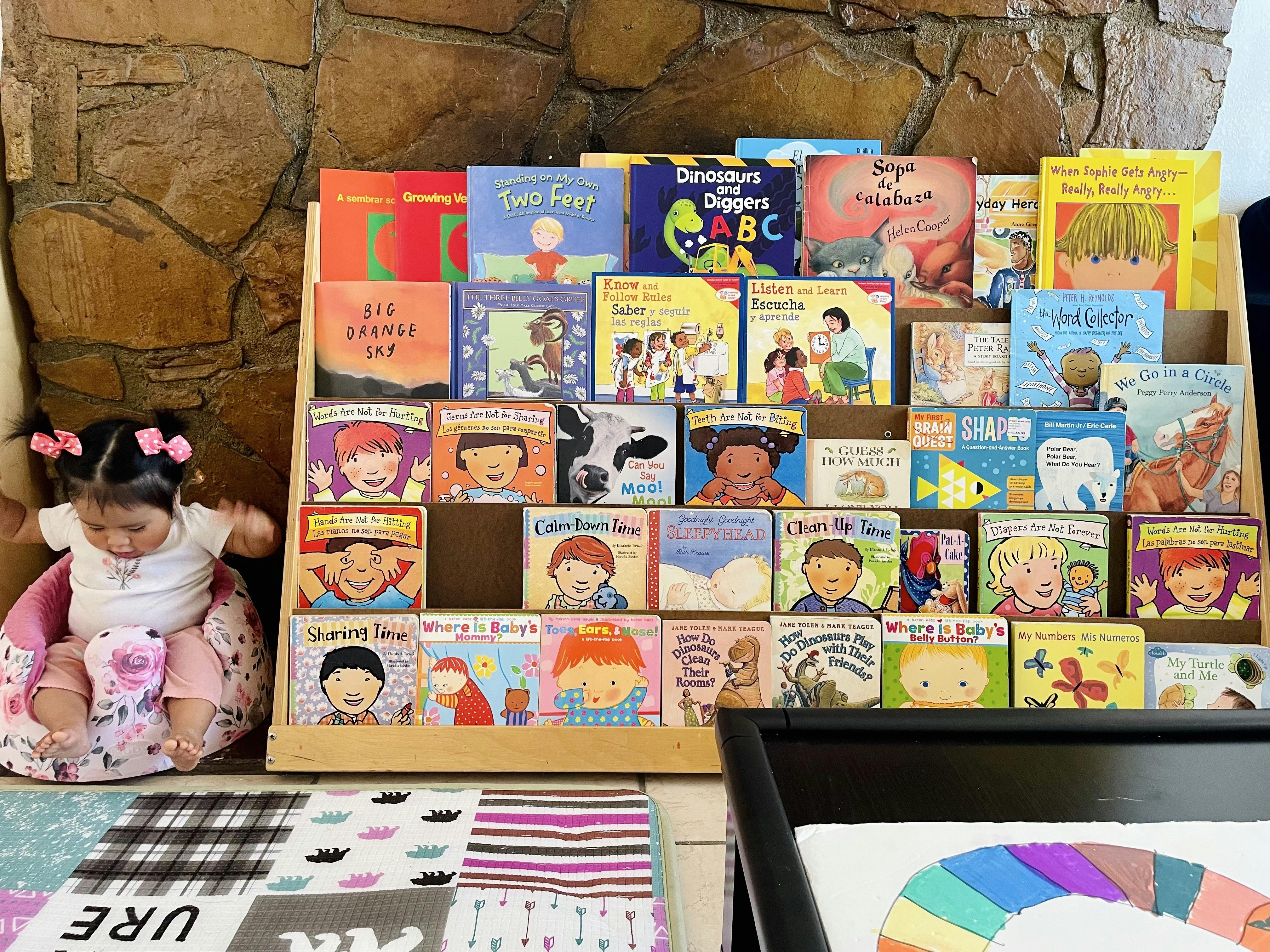 Child sitting in a pink chair next to a bookshelf filled with children's books