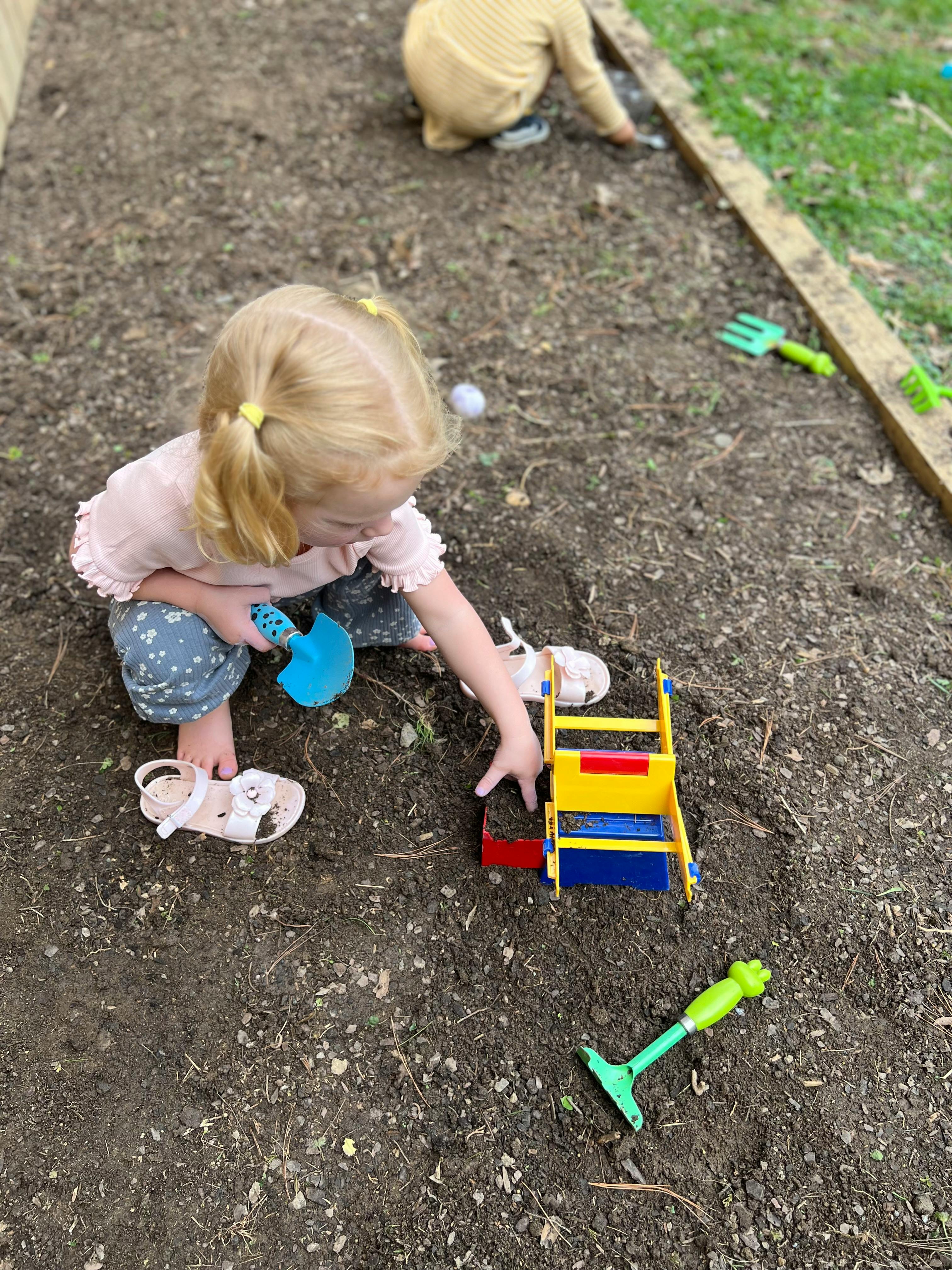 Child playing in dirt with toy shovel and wheelbarrow