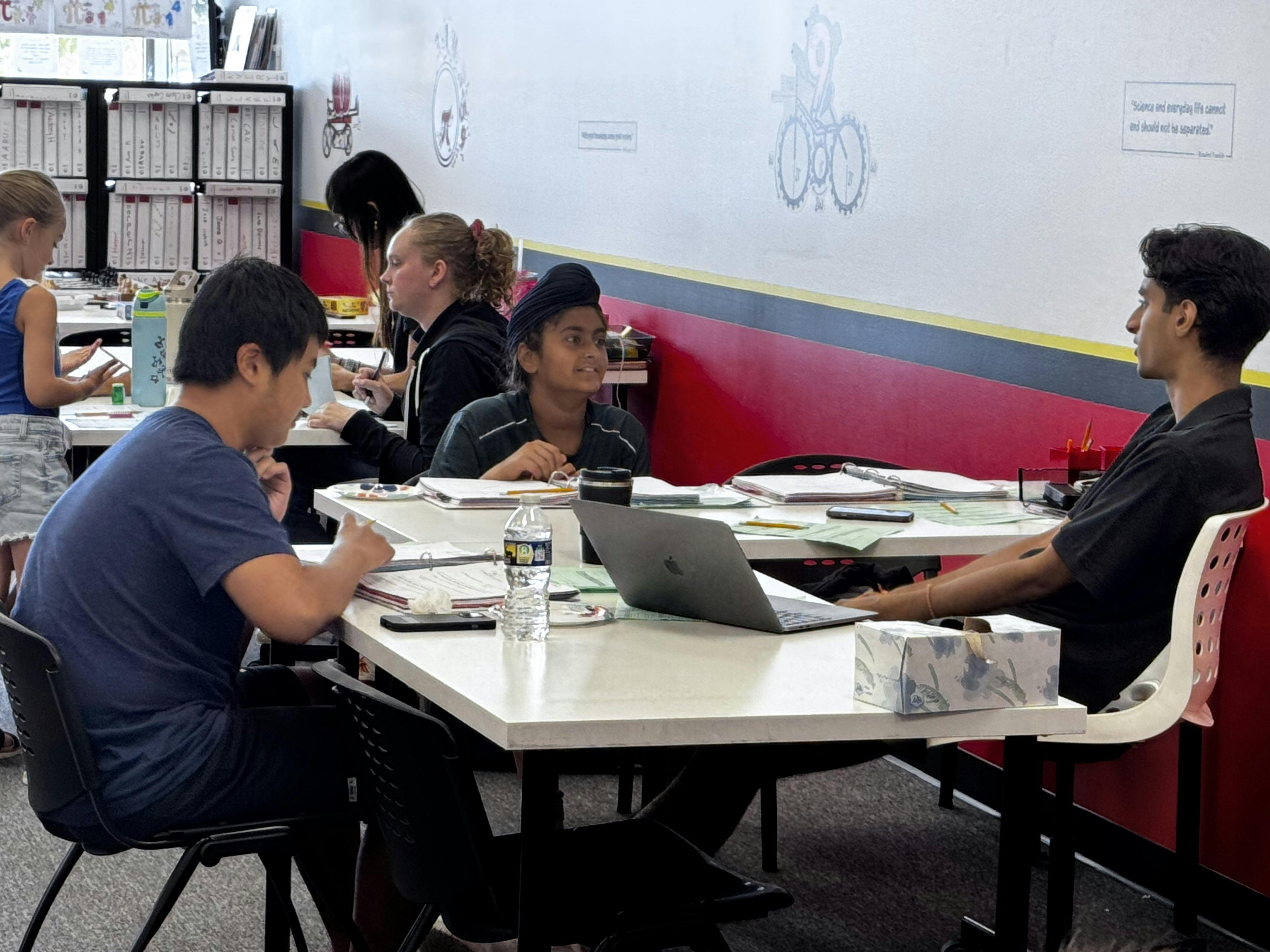 People sitting at tables with laptops and papers in a classroom