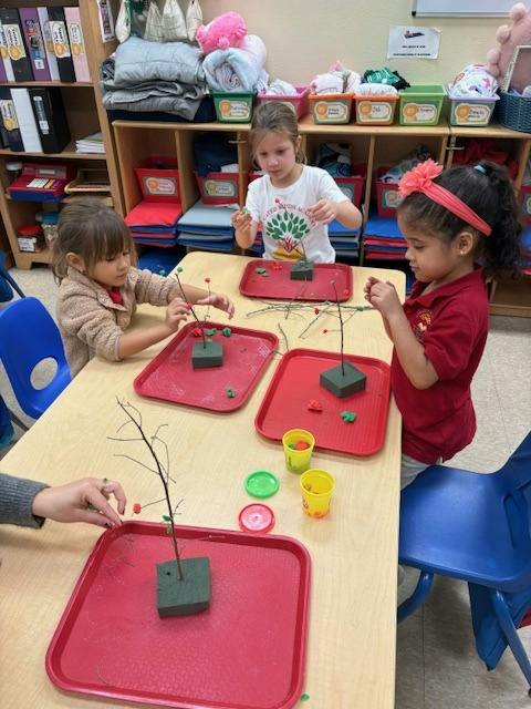 Children in a classroom making crafts with sticks and colorful clay on red trays
